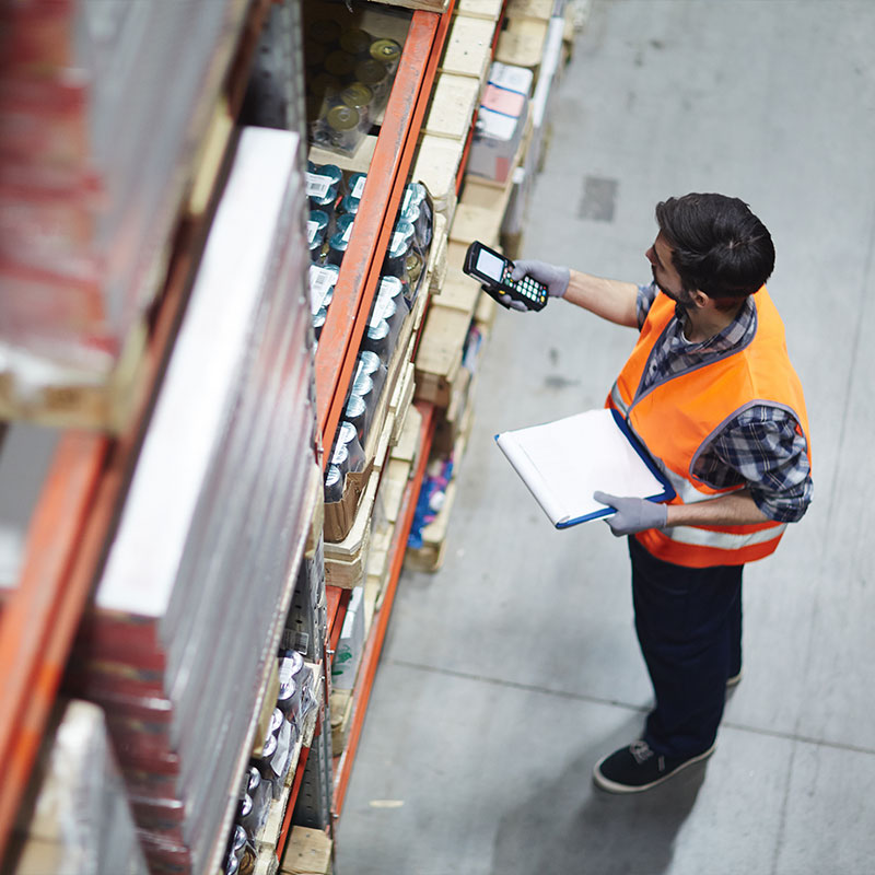 white man in a neon orange vest taking inventory in a warehouse